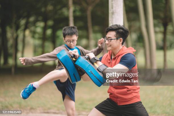 un athlète chinois asiatique de père formant son fils de 12 ans dans le stationnement public dans le kickboxing de soirée - concentration camp photos photos et images de collection