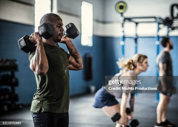 man lifting dumbells at cross training gym - body building stock pictures, royalty-free photos & images