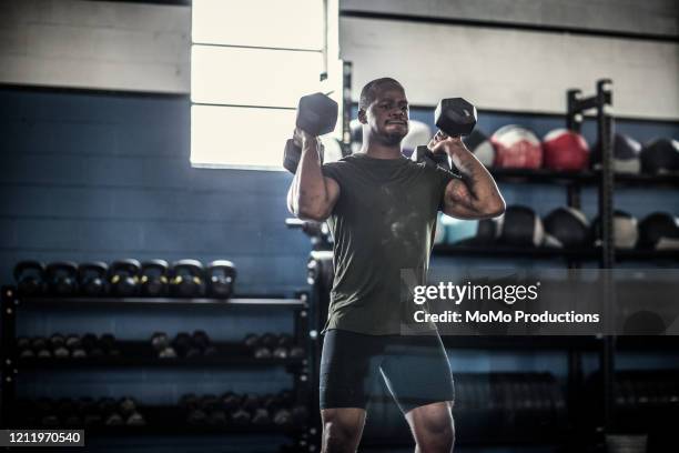 man lifting dumbells at cross training gym - lifting weights stock-fotos und bilder