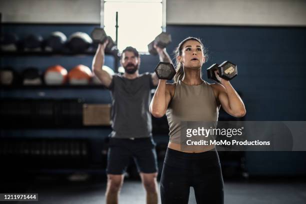 woman lifting dumbells at cross training gym - crossfit training fotografías e imágenes de stock