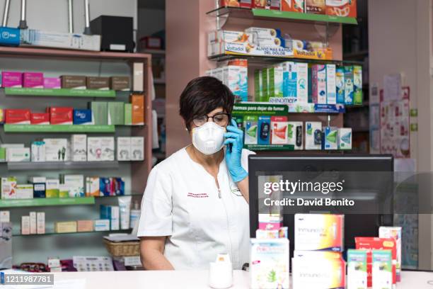 Pharmacist wearing a face mask talks on a phone at a pharmacy in Alpedrete in the Community of Madrid on March 12, 2020 in Madrid, Spain. Yesterday,...