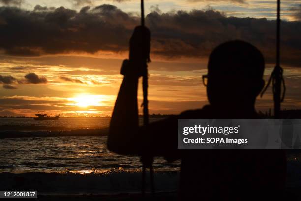 Silhouette of a man on a swing watching the sunset at Susoh beach.