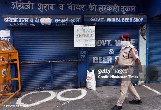Police personnel stands guard outside a liquor shop shut with a notice reading that the 'shop will remain closed till further notice' pasted on its...