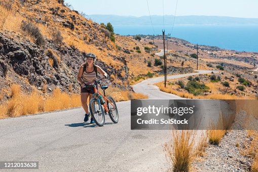 Woman wheeling bicycle uphill on winding road