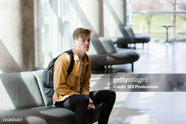 young adult male student sits in lobby waiting for ride - star style lounge imagens e fotografias de stock
