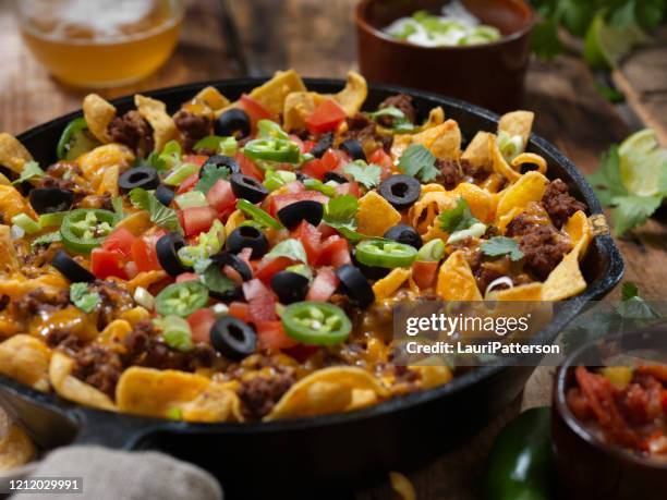 baked frito pie (chili corn chip nachos) with black olives, tomatoes, green onions, jalapenos, salsa, guacamole and sour cream - nacho chip stock pictures, royalty-free photos & images