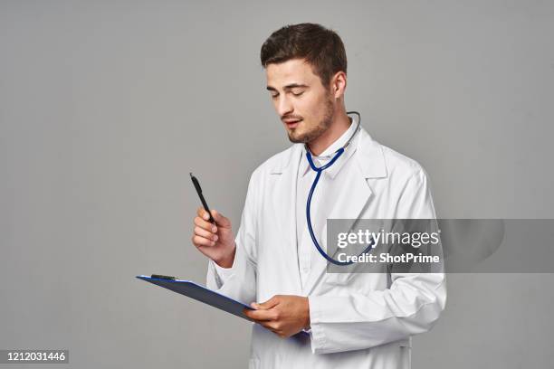 a doctor in a white coat and a stethoscope on his neck write down the results of medical tests on a tablet. - patient history stock pictures, royalty-free photos & images