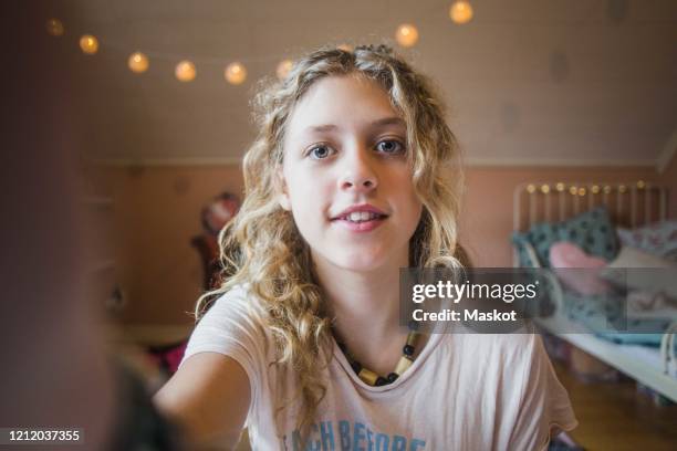 portrait of girl with blond hair taking selfie while sitting in bedroom - selfie imagens e fotografias de stock