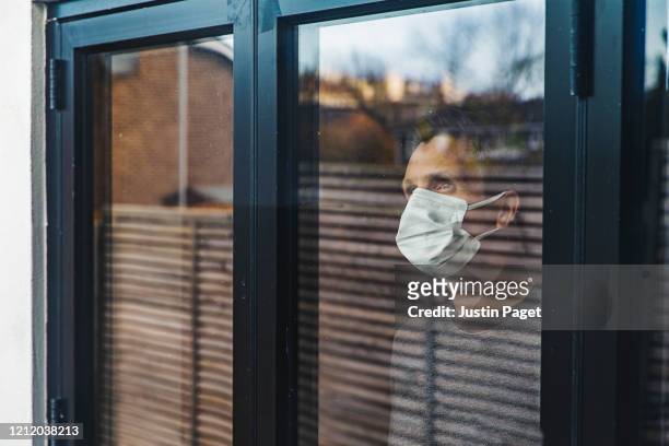 man with mask looking out of window - quarantäne stock-fotos und bilder
