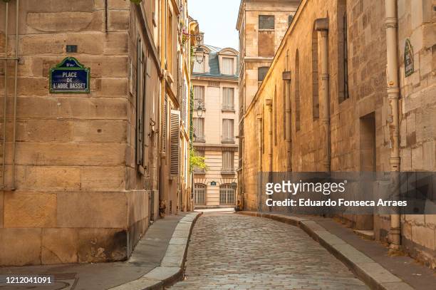 a narrow cobblestone street in the old city of paris, lined by stone buildings and illuminated by the sunlight. - alley fotografías e imágenes de stock
