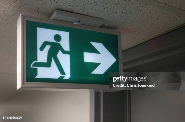 emergency exit sign pointing to door - evacuación fotografías e imágenes de stock