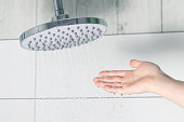 Female hand touching water pouring from a rain shower head, checking water temperature