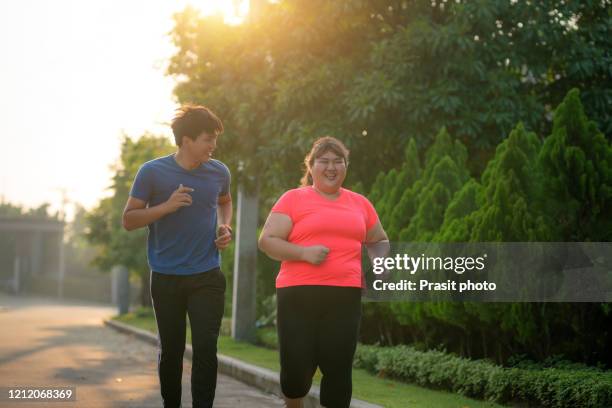 two asian trainer man and overweight woman exercising together in public park in village, jogging or power walking, laughing and conversation in morning during sunlight. fat women take care of health and want to lose weight concept. - fat couple photos et images de collection
