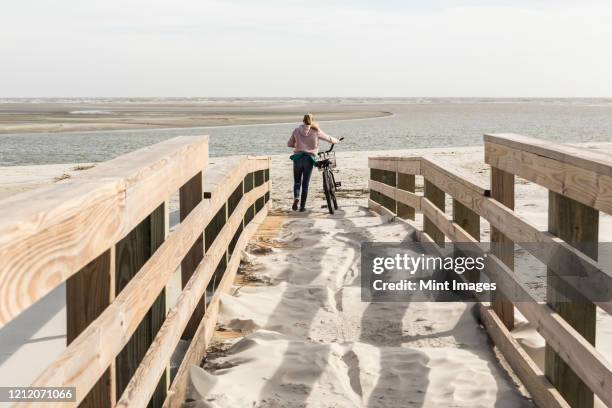 teenage girl on her bicycle crossing bridge to the beach - bois flotté photos et images de collection