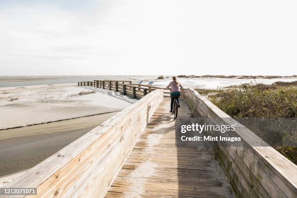 teenage girl on her bicycle crossing bridge to the beach - bois flotté photos et images de collection