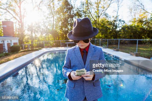 boy in a suit and dark glasses standing on the edge of water counting dollar bills. - boys money stock pictures, royalty-free photos & images