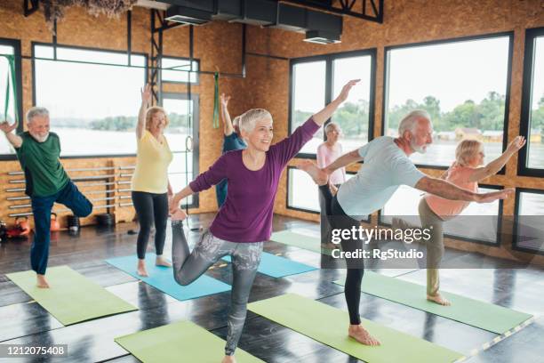 group of seniors practicing balance on the yoga class - active mature adult stock pictures, royalty-free photos & images