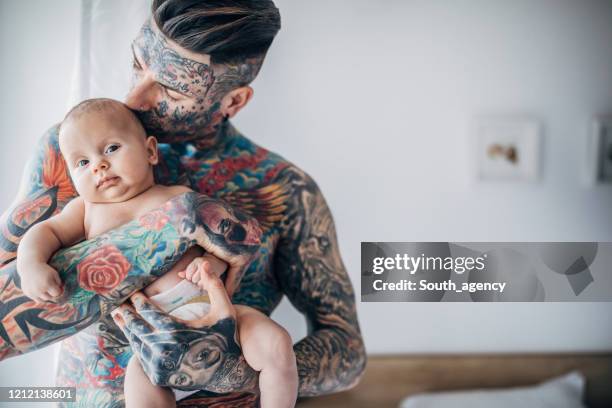 young father with whole body in covered in tattoos holding his baby son in bedroom - a separate peace stock pictures, royalty-free photos & images