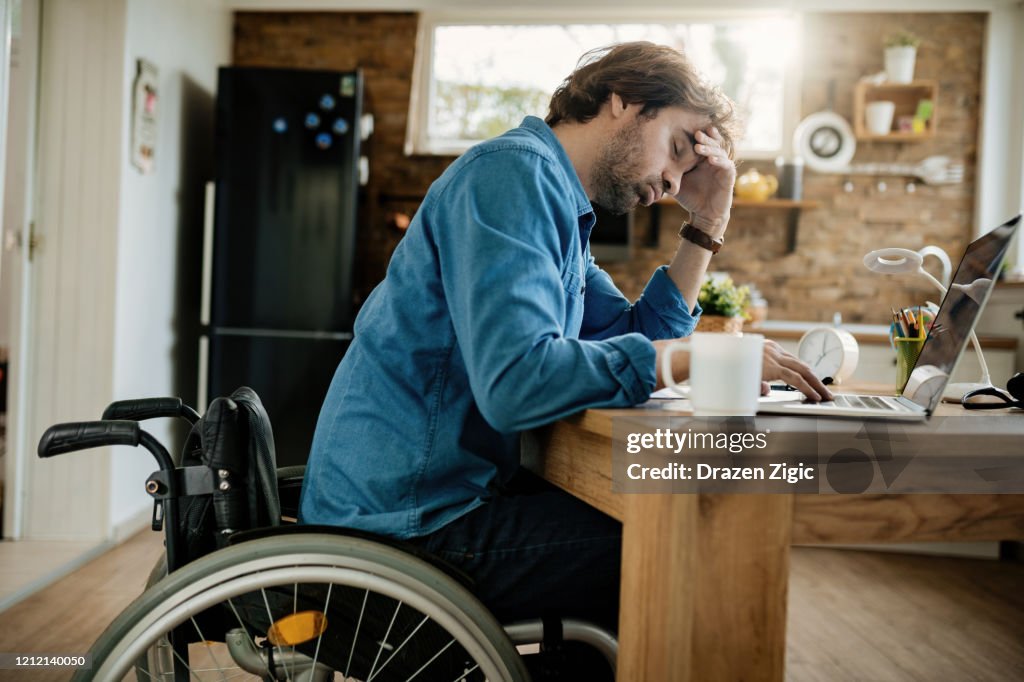 Hieronder mening van uitgeputte freelancer in rolstoel die op laptop thuis werkt.