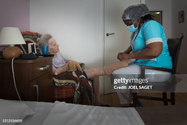 Nurse assists Nicole Muller with her clothes in her bedroom at the Camille Saint-Saens EHPAD in Aulnay-sous-Bois, a Paris suburb, on May 6 on the...