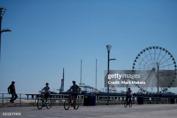 Mean wearing a mask sits on the boardwalk railing as cyclists pedal past during the coronavirus pandemic on May 7, 2020 in Atlantic City, New Jersey....