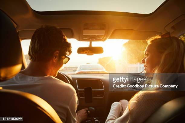 smiling young couple driving in their car in the late afternoon - car sunset stock pictures, royalty-free photos & images