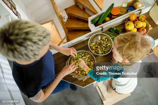 Symbolic picture on the subject of family life: A woman and an infant stand together in the kitchen and cover a cake with fruit on May 03, 2020 in...