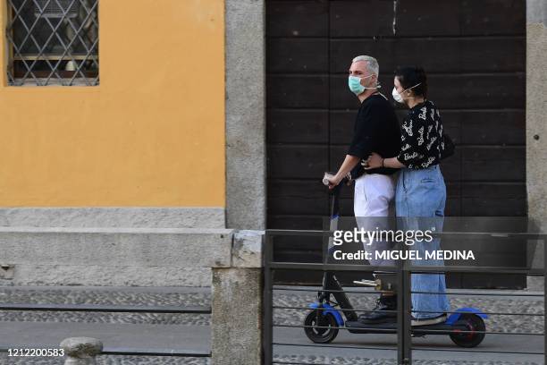 Couple wearing a face mask rides an electric scooter along a Navigli canal in Milan on May 8, 2020 during the country's lockdown aimed at curbing the...