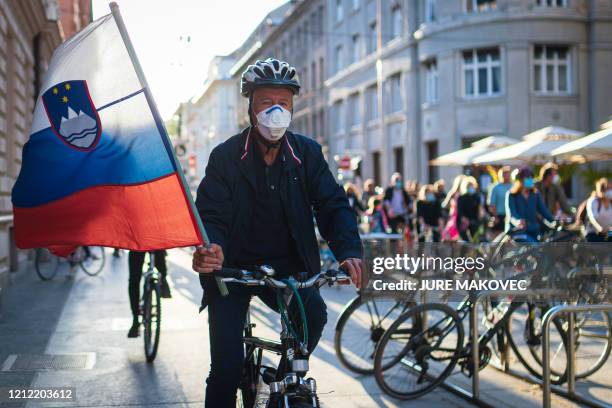 Slovenian citizen, wearing protective masks, holds a Slovenian flag as he and others ride their bikes as they block the centre of capital Ljubljana...