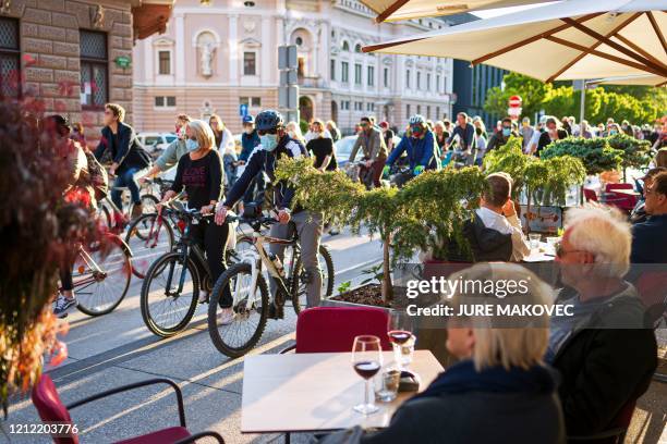 People having drinks on terraces look at Slovenian citizens, some wearing protective masks, riding their bikes as they block the centre of capital...