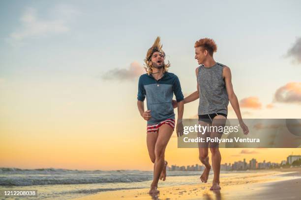 personnes courant sur la plage au coucher du soleil - gay men swimwear photos et images de collection