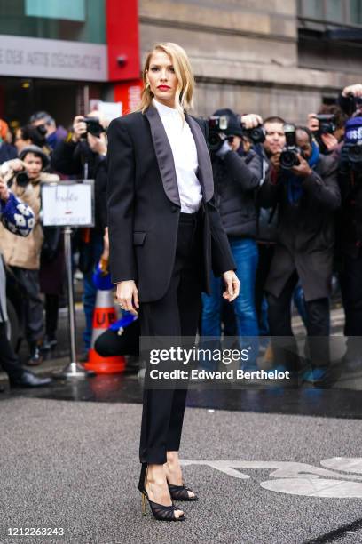 Lena Perminova wears earrings, a white shirt with a mandarin-collar, a black tuxedo jacket, black pants, black peep-toe heeled sandals, outside...