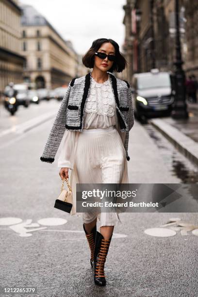 Chriselle Lim wears sunglasses, a heather black tweed crop jacket with a black trim, a white lace gathered long sleeved top, a white flowing pleated...