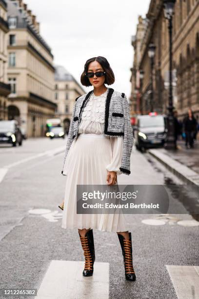 Chriselle Lim wears sunglasses, a heather black tweed crop jacket with a black trim, a white lace gathered long sleeved top, a white flowing pleated...