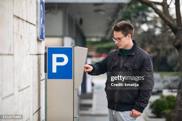 young adult man paying parking meter on city street - parking sign stock pictures, royalty-free photos & images