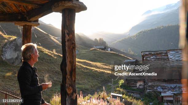 mature man relaxes outside mountain hut at sunrise - hut stock pictures, royalty-free photos & images