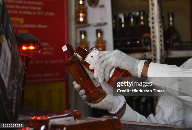 Sales person wearing surgical gloves scans alcohol bottles at a liquor shop in Nazafgarh, on May 8, 2020 in New Delhi, India.