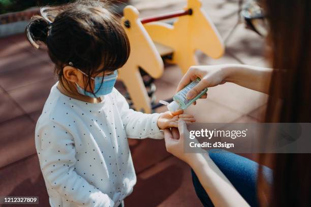 young mother squeezing hand sanitizer onto little daughter's hand in the playground to prevent the spread of viruses - antiseptic stock-fotos und bilder