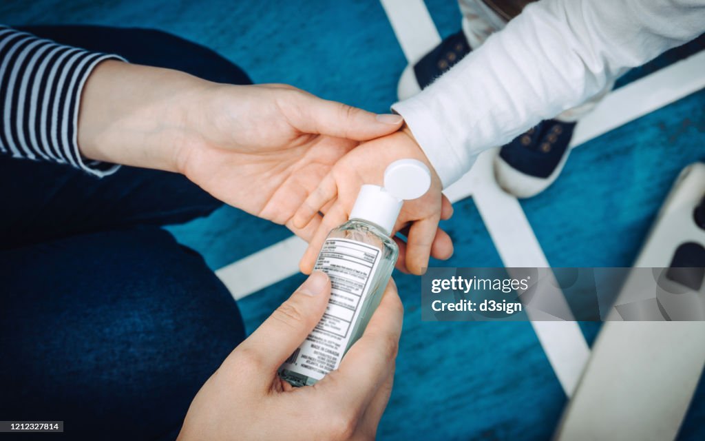 Overhead view of young mother squeezing hand sanitizer onto little daughter's hand in the playground to prevent the spread of viruses