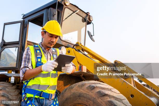 driving worker heavy wheeled tractor, workers drive orders through the tablet computer, wheel loader excavator with backhoe unloading sand works in construction site. - heavy equipment stock pictures, royalty-free photos & images