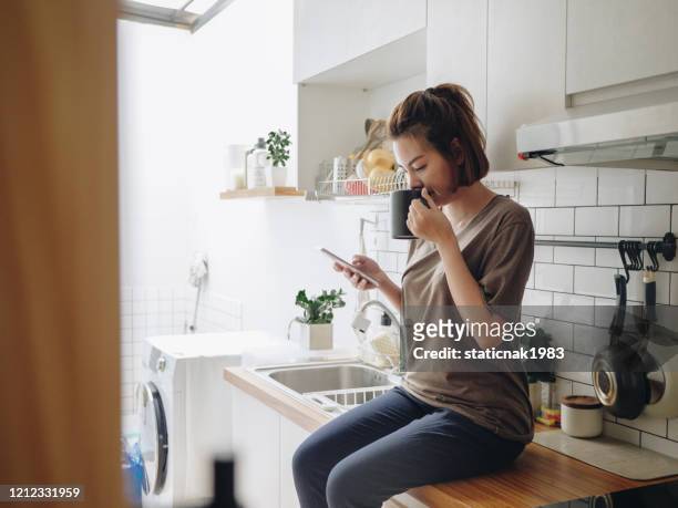 jonge vrouwenzitting in gezellige keuken en het werken op haar mobiel. - mobile device on table stockfoto's en -beelden