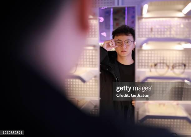young man choosing glasses in optical shop - ge healthcare stock pictures, royalty-free photos & images