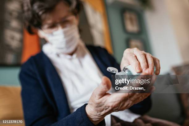 hogere vrouw die handontsmettingsmiddel thuis toepast - handdesinfectiemiddel stockfoto's en -beelden