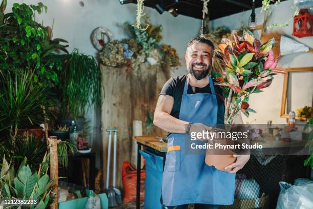lächelnder gärtner arbeitet mit blumen im gartencenter - florist stock-fotos und bilder