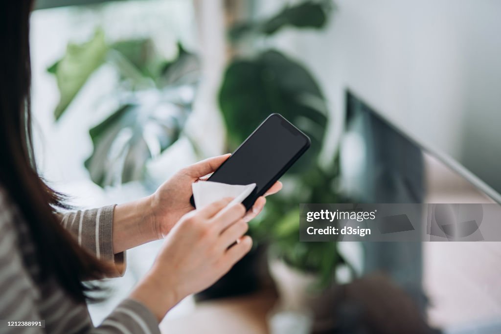 Cropped shot of a young woman cleaning the surface of smartphone with antibacterial tissue at home