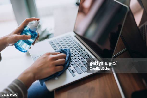 cropped shot of a young woman cleaning the surface of laptop with cleaning spray and antistatic cloth at home - antiseptikum stock-fotos und bilder