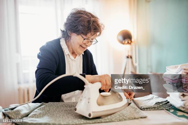 seniorin bügelt und macht hausarbeiten - bügelbrett stock-fotos und bilder