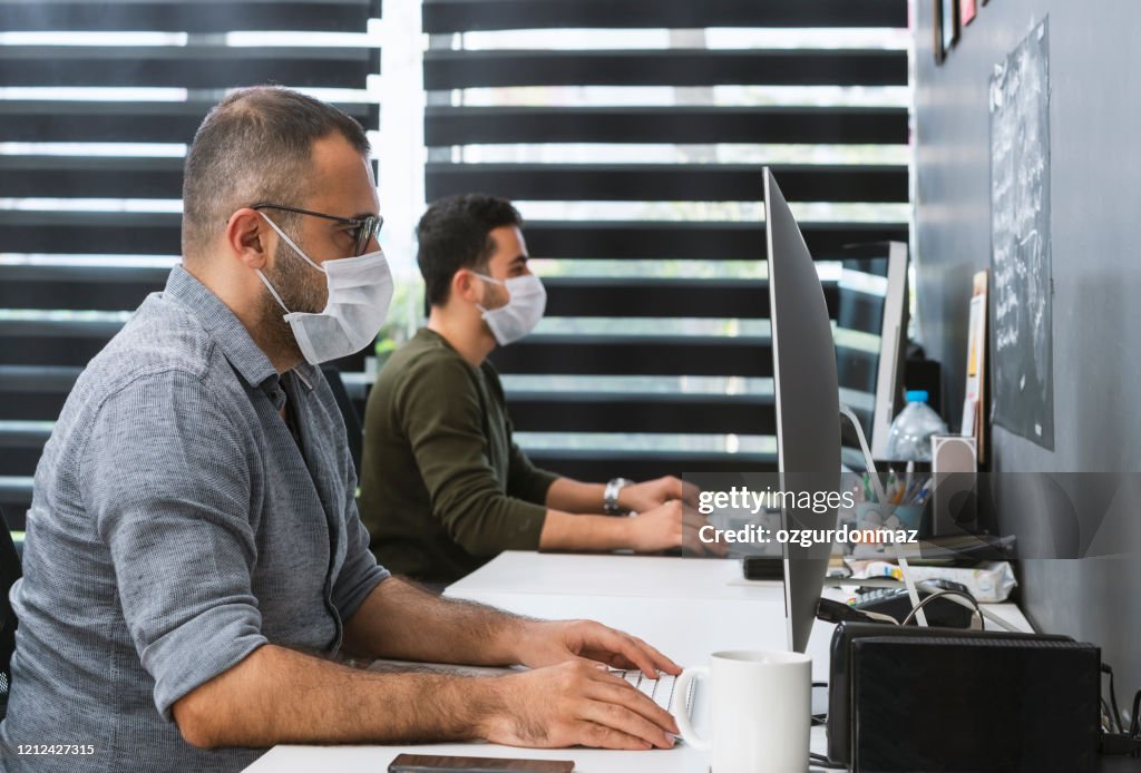 Dos hombres de negocios con máscaras protectoras están trabajando en la oficina