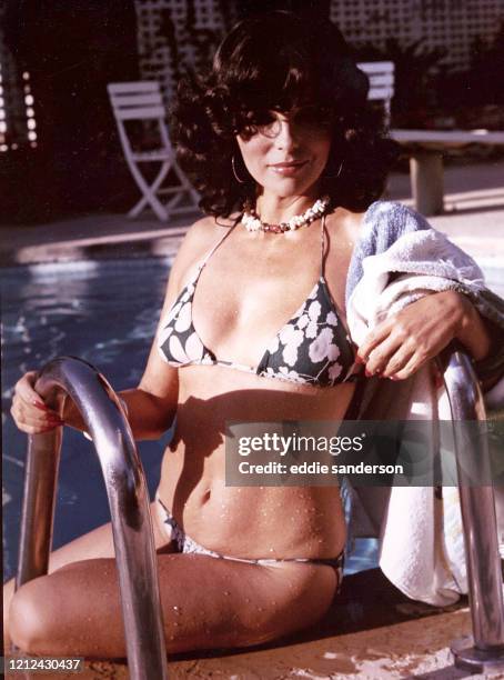 Actress Joan Collins wearing a floral print bikini sitting at the side of the pool at her Beverly Hills, California home in June 1976..