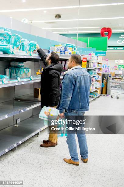 Two men reach for items as consumers leave shelves empty in a London Morrisons store as panic-buying over coronavirus continues on March 14, 2020 in...